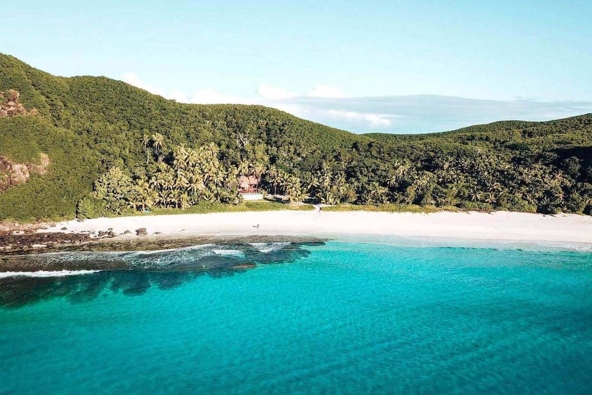A view across teal coloured water towards a deserted, paradise island
