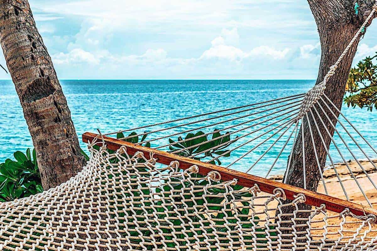 A close up of a hammock between trees next to calm blue sea in Fiji