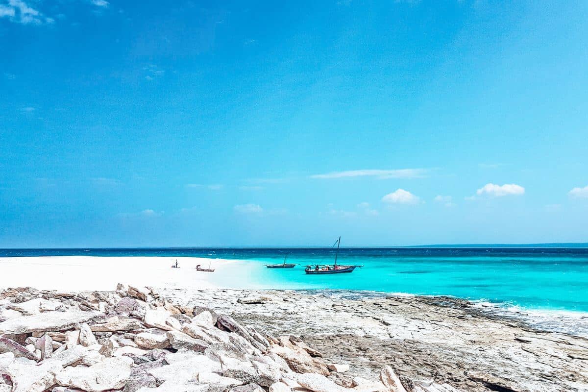 A brilliant white sandy beach with bright blue waters and traditional boats in Mozambique