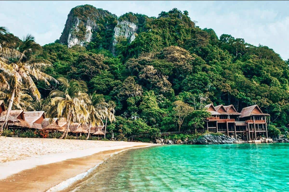 A tropical palm-fringed beach in Palawan framed by dramatic limestone mountains