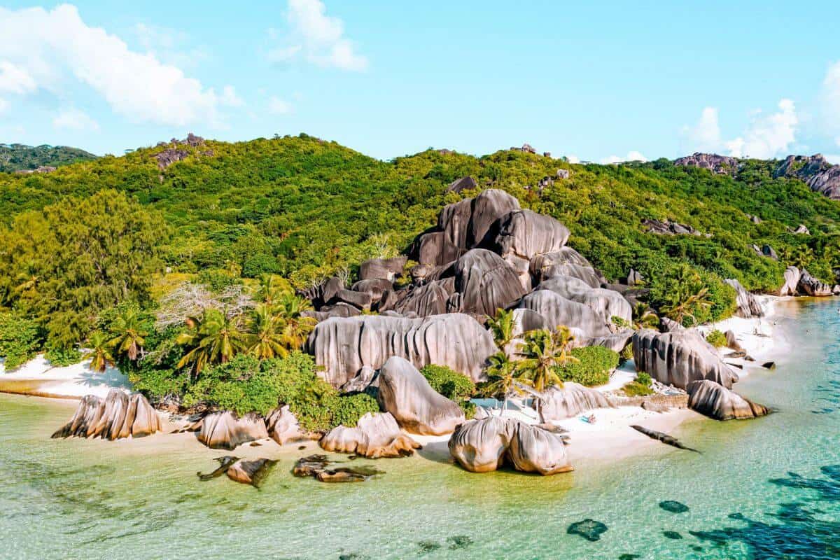 A view over the sea towards a tropical beach with granite boulders and palm trees