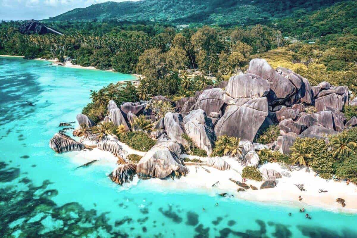 A view of granite rocks and jungle beside a white-sand beach and turquoise sea in the Seychelles