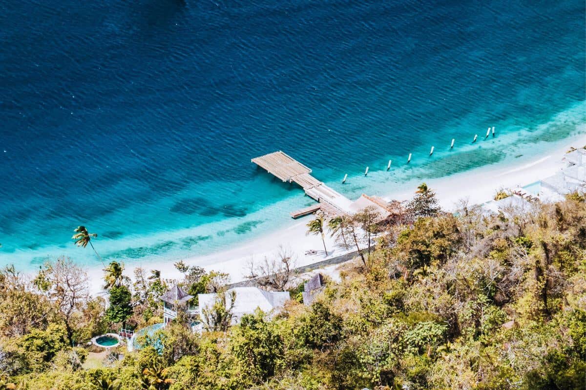 An aerial view of a white sandy, tropical coastline with a jetty jutting into the sea
