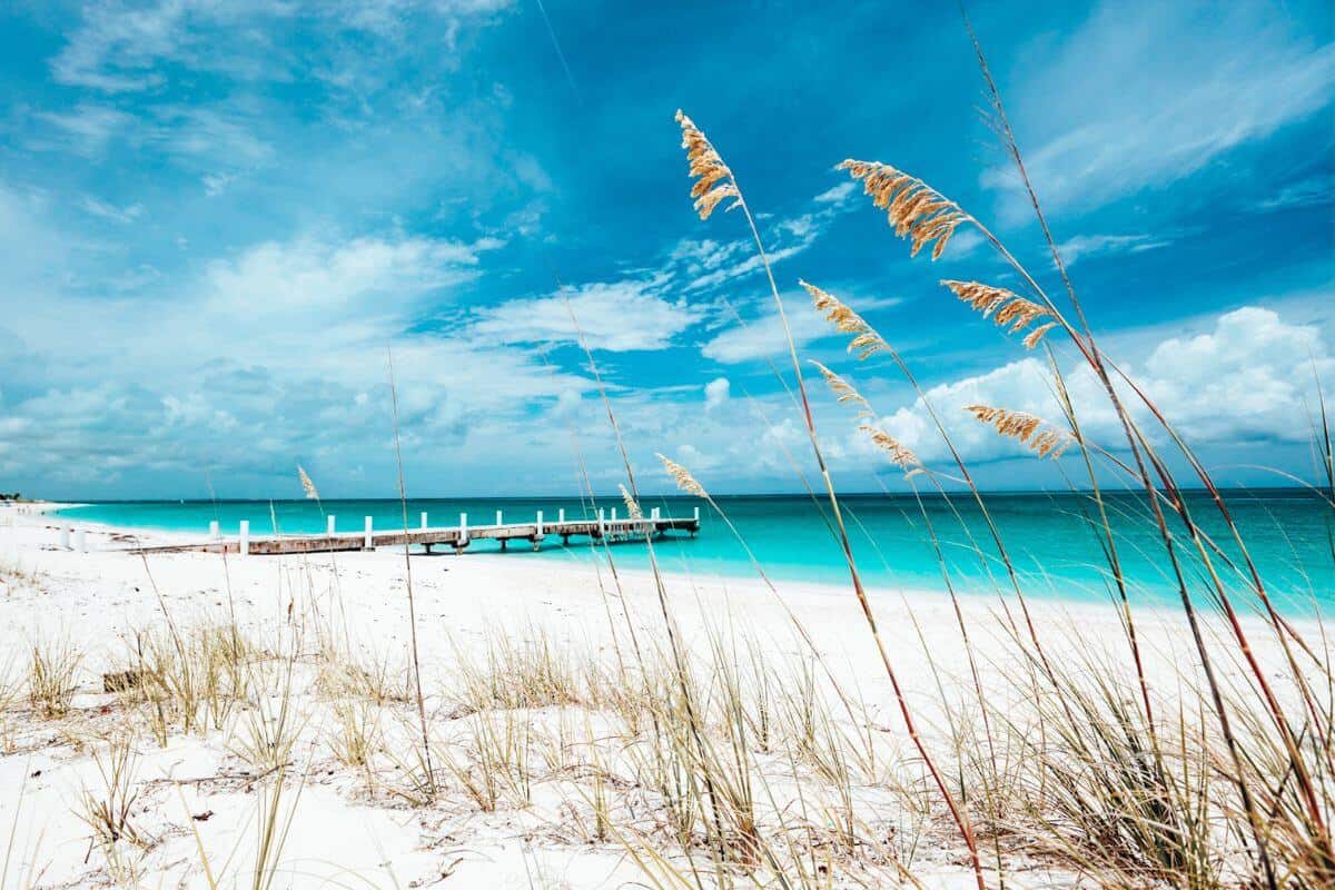 A bright white sandy beach in the Caribbean with a jetty jutting into turquoise sea