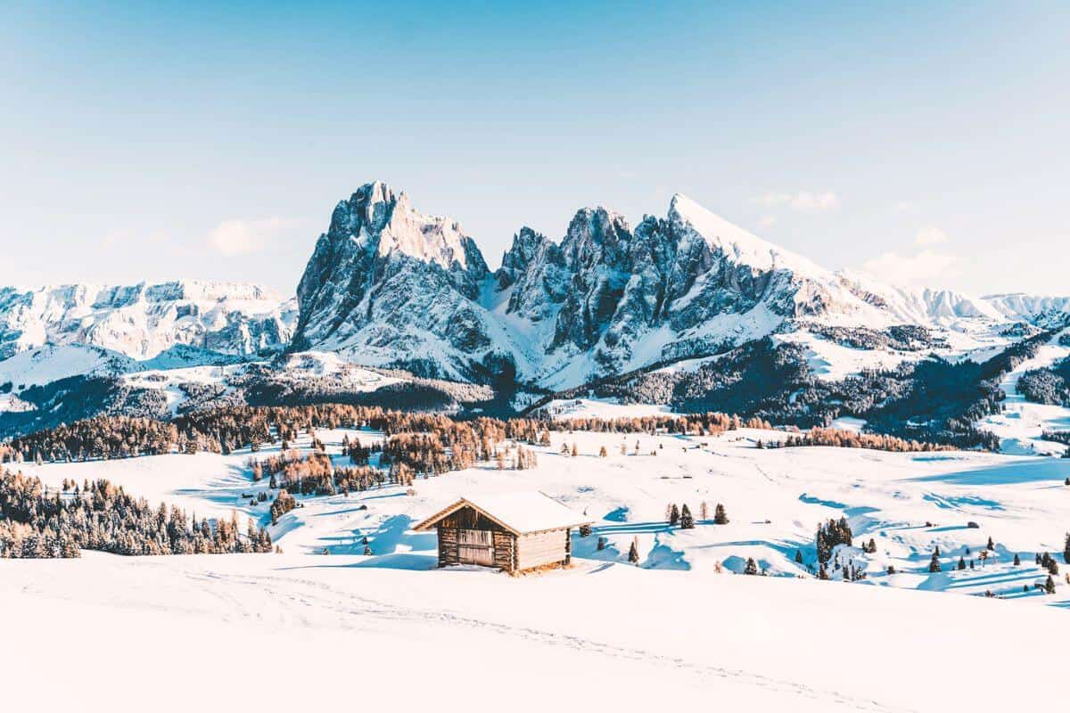 A wooden hut set in an idyllic winter landscape in front of snowy mountains and forests