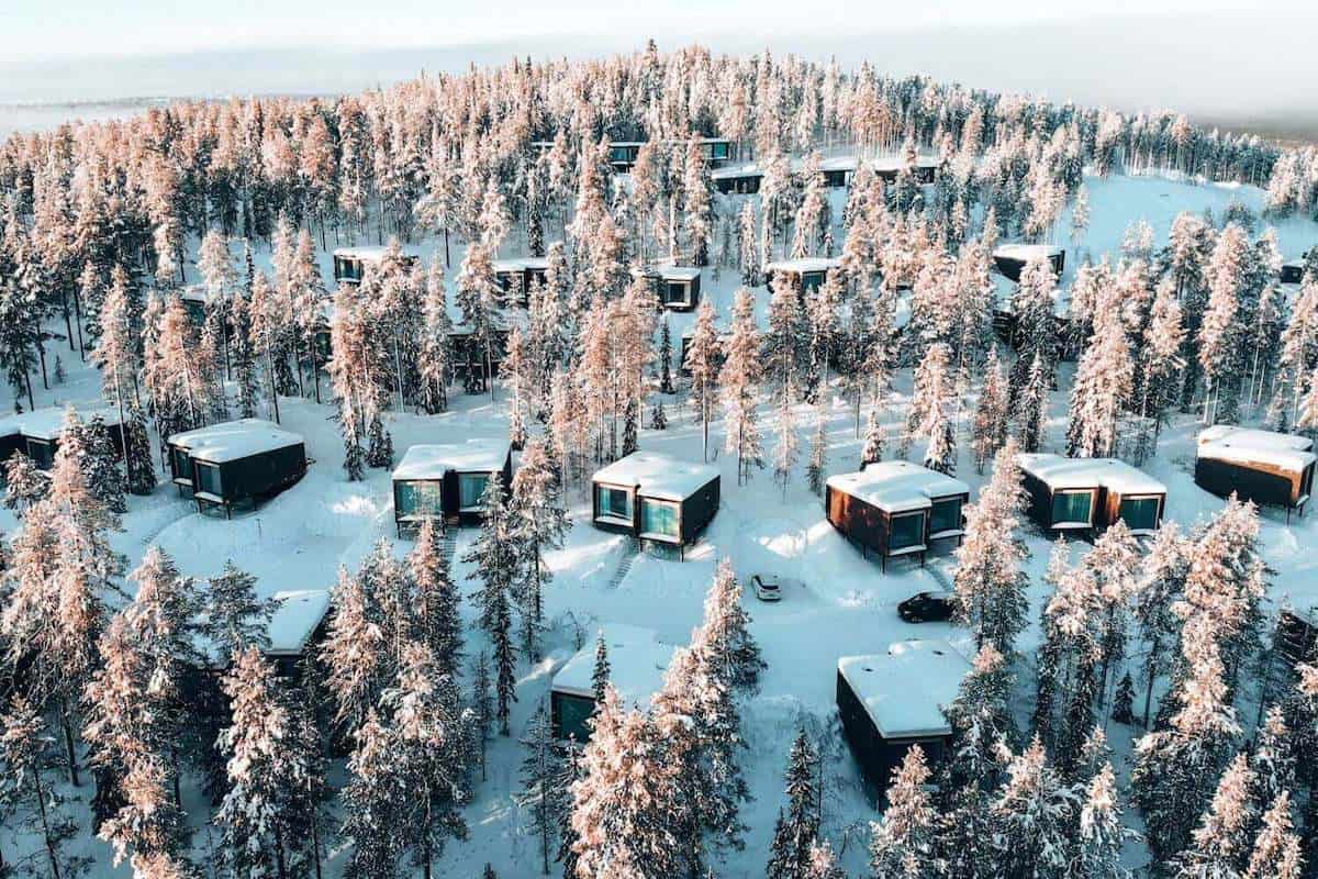 Several small wooden cabins set amongst a snowy forest in remote Lapland