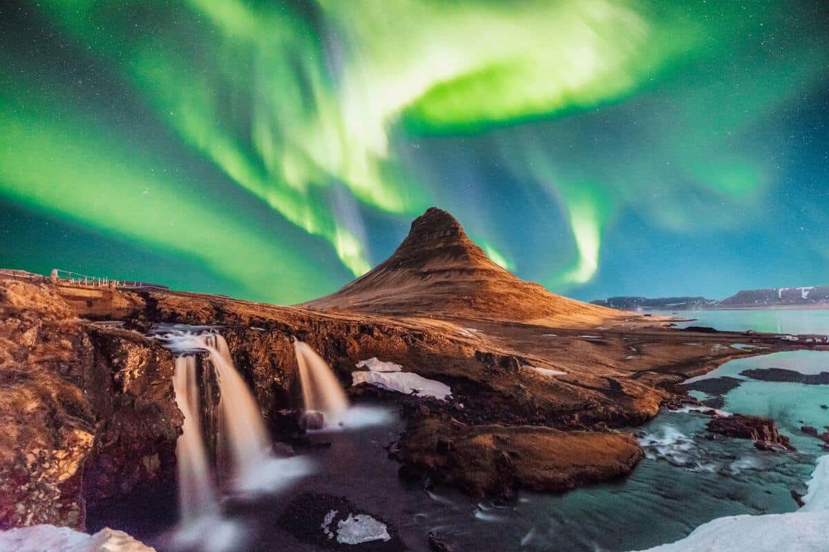 A rugged mountainous landscape in Iceland with frozen waterfalls under the Northern Lights