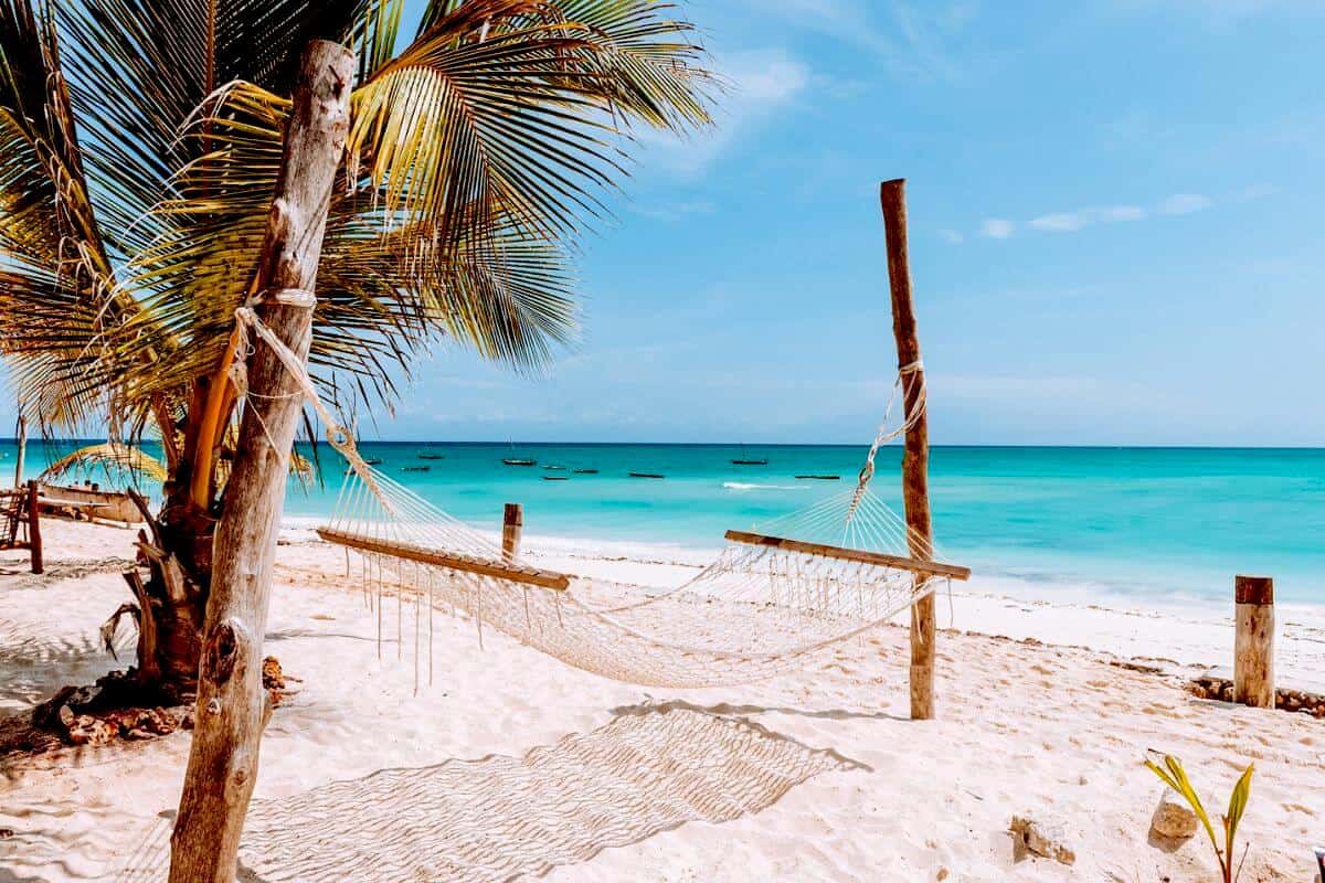 A hammock and palm trees on a pristine white sandy beach in Zanzibar with turquoise waters