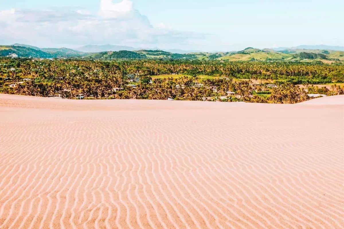 A view across sand dunes in Fiji with green tropical scenery in the background