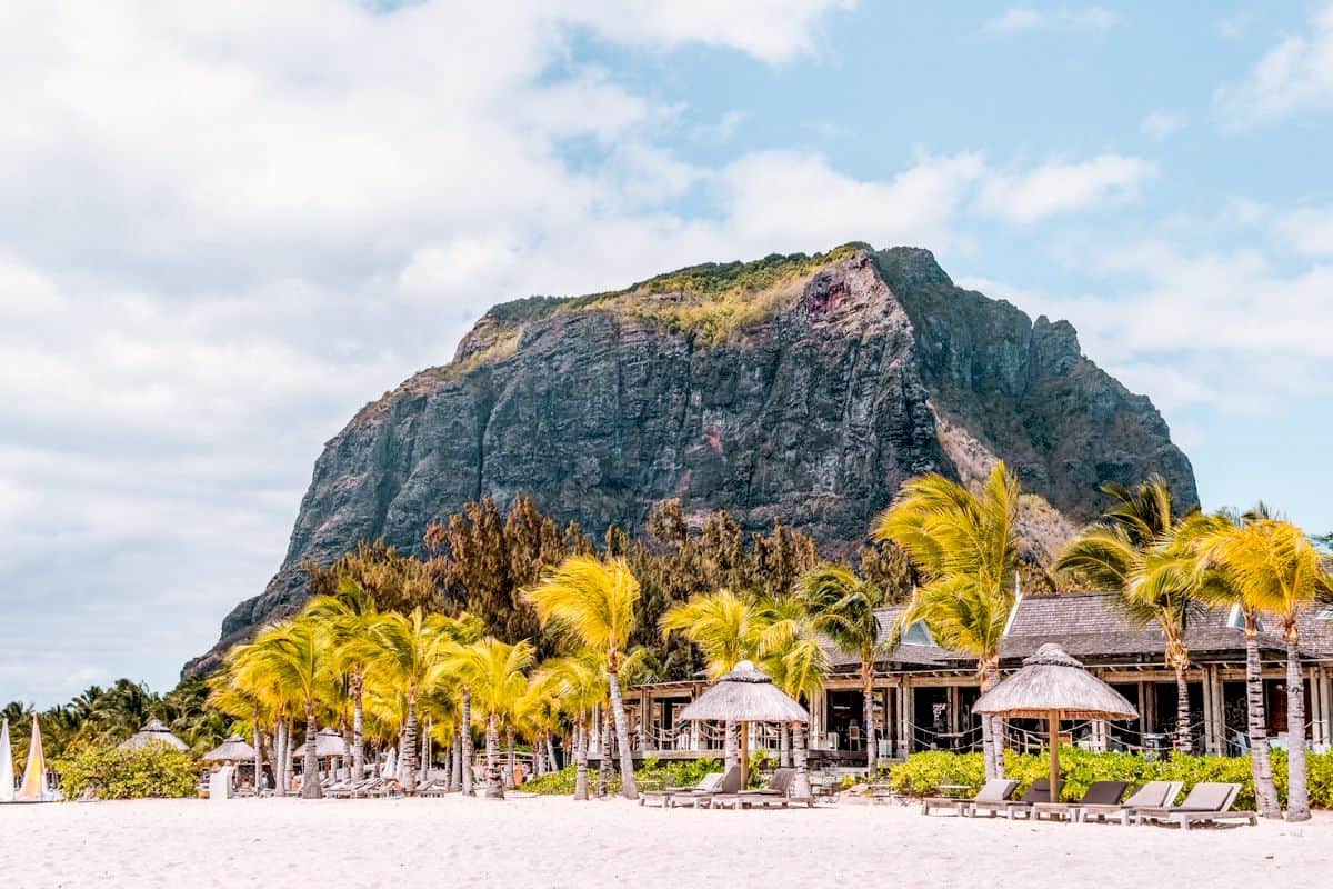 A tropical beach resort in Mauritius with palm trees set in front of a towering, dramatic mountain