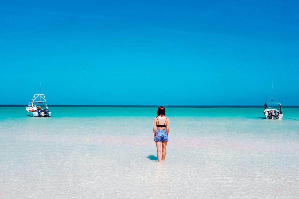 A woman (me!) walking out into shallow, crystal clear waters from a beach in Isla Holbox, Mexico