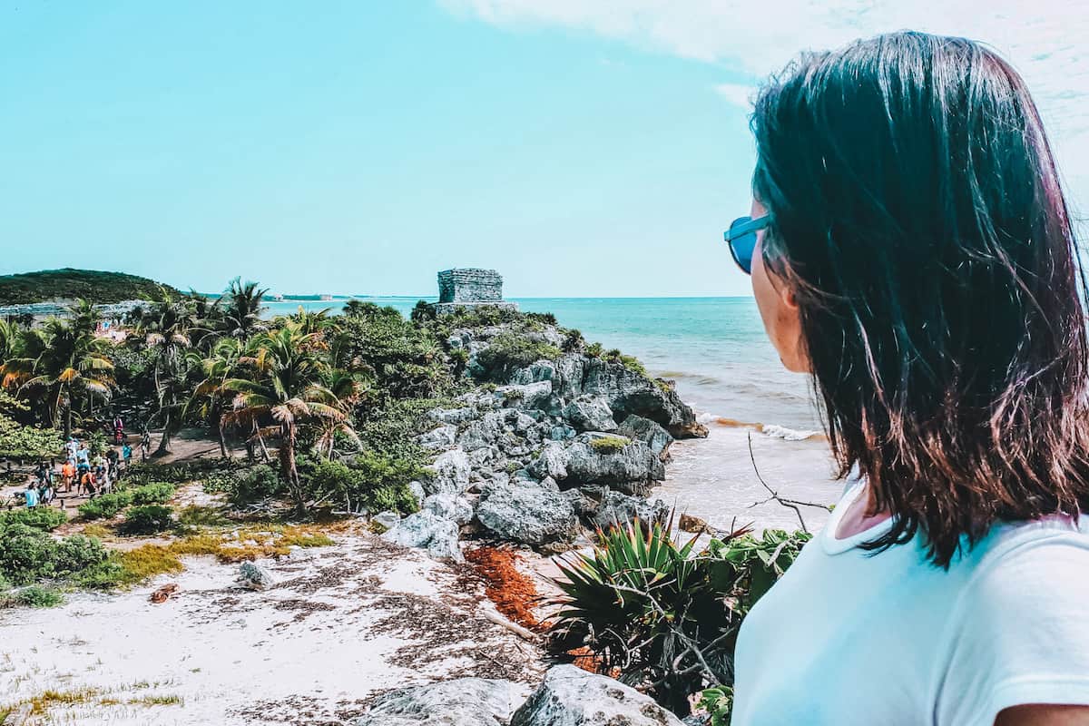 A woman (me!) looking towards a Mayan ruin on the tropical coast of Tulum in Mexico
