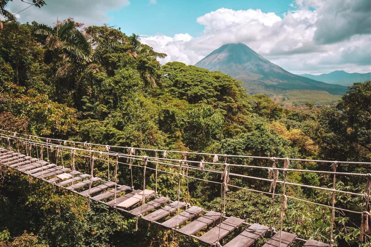A wooden suspension bridge across the rainforest in Costa Rica with a volcano in the background