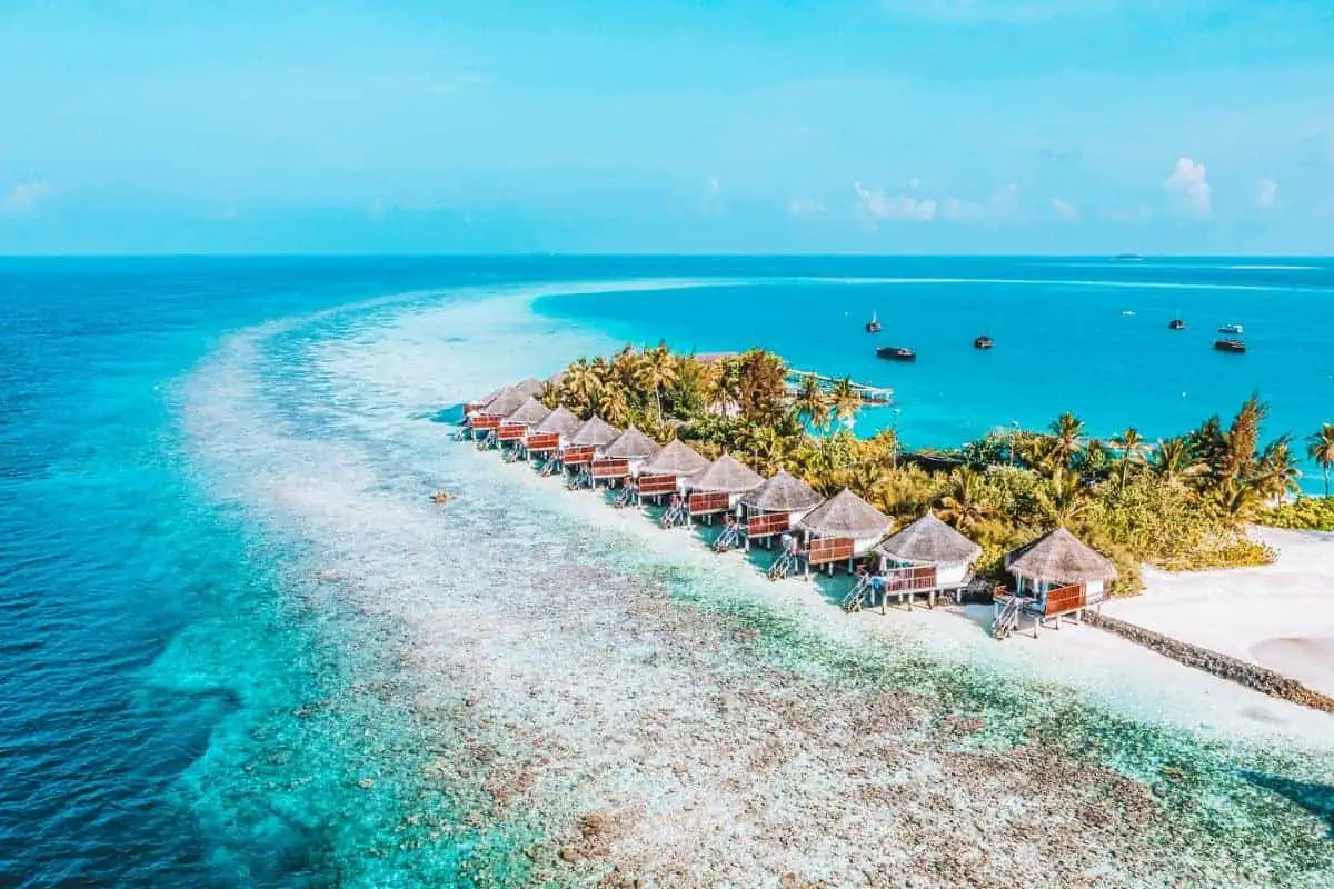 An aerial view of a small, tropical private island resort in the Maldives with overwater villas
