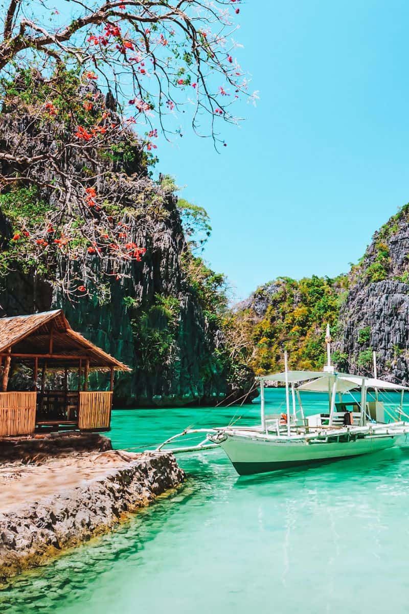 A traditional banca boat in bright turquoise water in the Philippines, surrounded by limestone cliffs