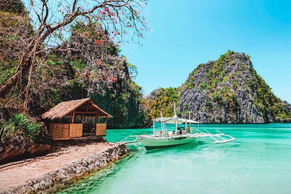 A traditional banca boat in bright turquoise water in the Philippines, surrounded by limestone cliffs