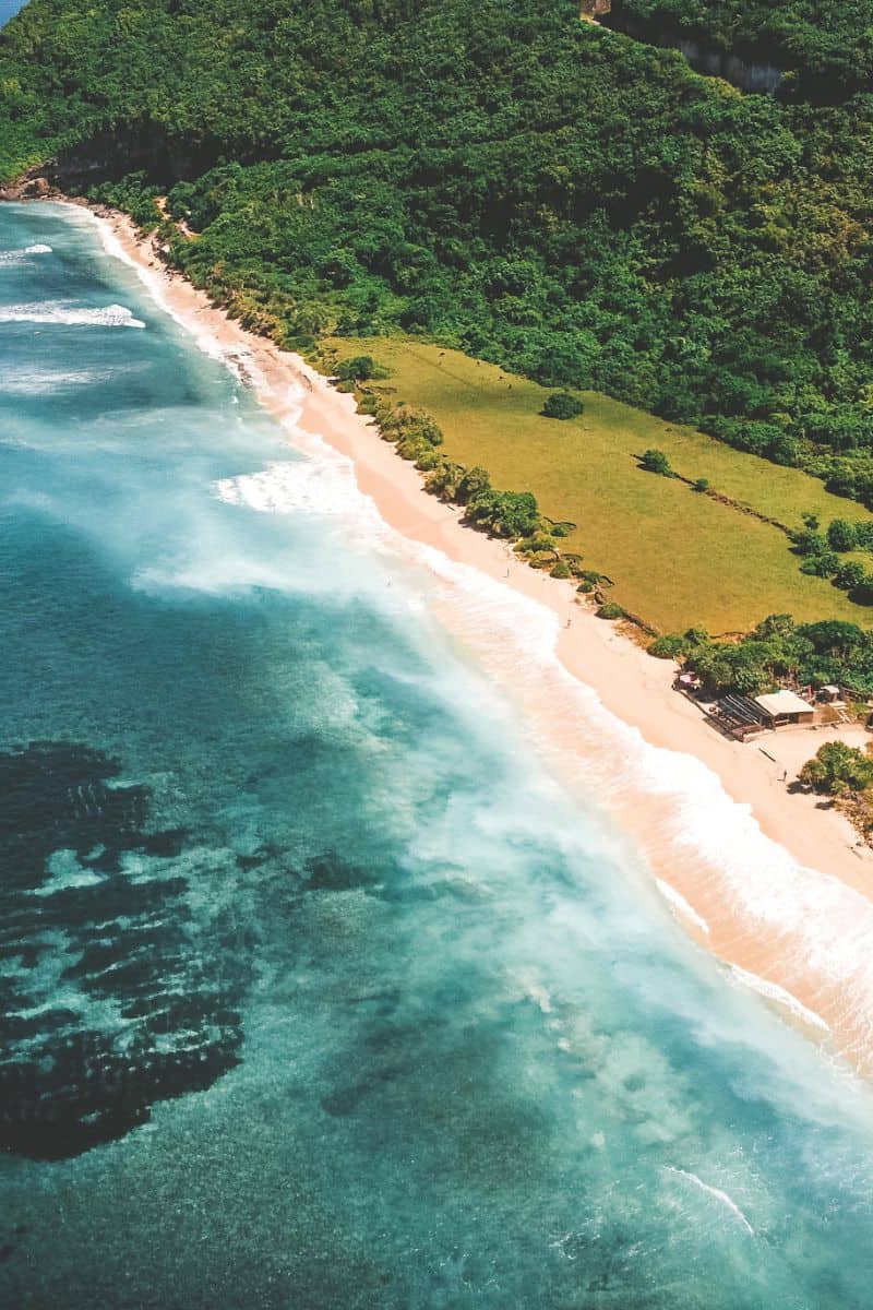 An aerial view of an empty, sandy beach in Uluwatu, Bali