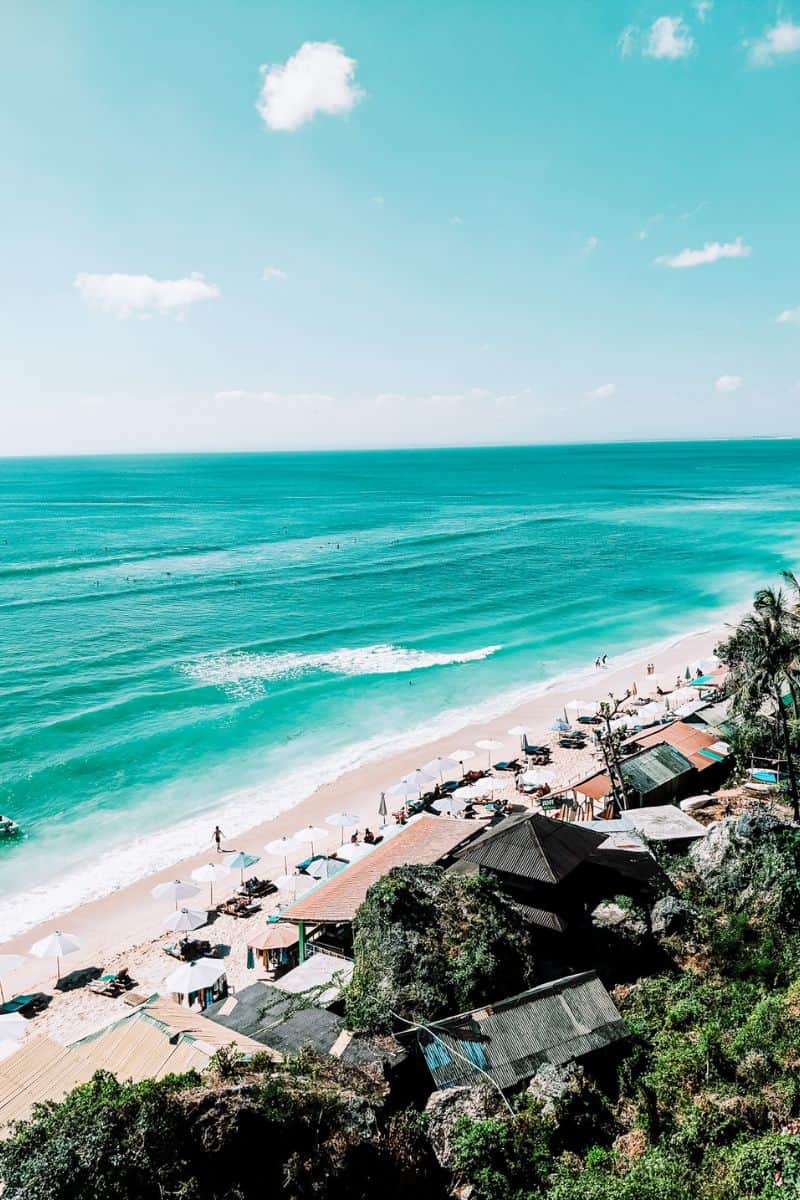 A view along a stretching coastline in Bali with people on the beach and in the water