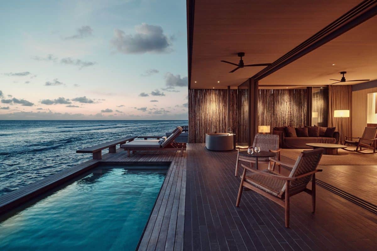A view towards a sunset over the ocean from a modern overwater villa with a private pool at Patina Maldives resort
