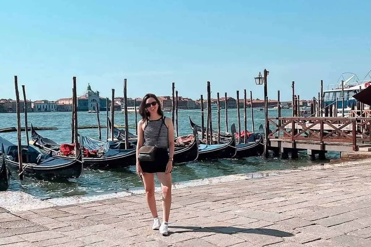 Hannah standing in front of gondolas by St Mark's Square in Venice