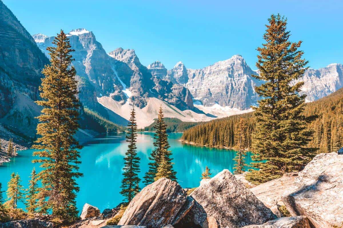 A brilliant blue lake in Canada surrounded by mountains and pine trees on a bright sunny day