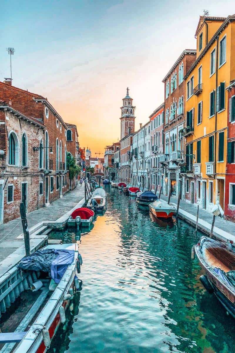 A canal in Venice between colourful buildings with boats moored on either side 