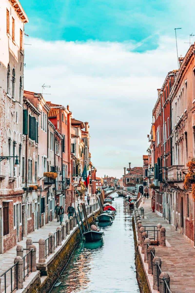 A narrow canal between pavements and pastel coloured houses in Venice