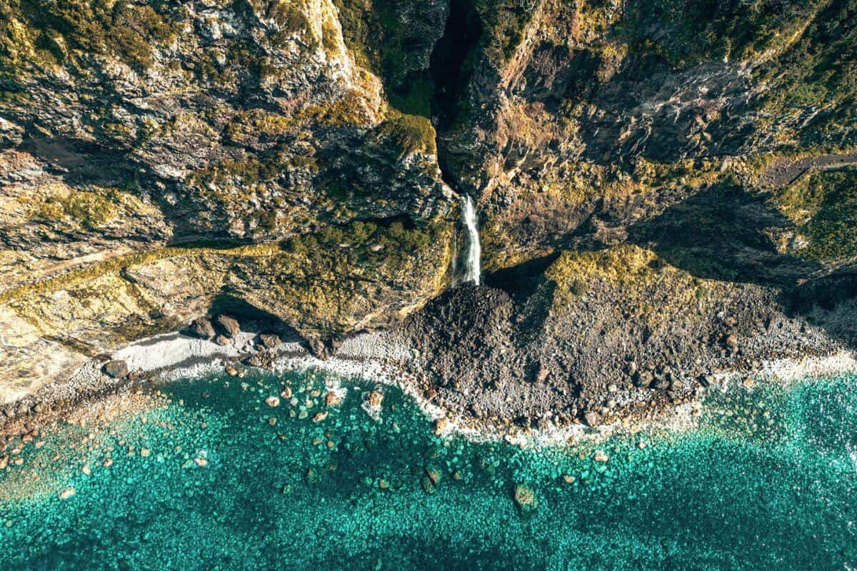 An aerial view of a rugged cliffside with a waterfall spilling into the ocean