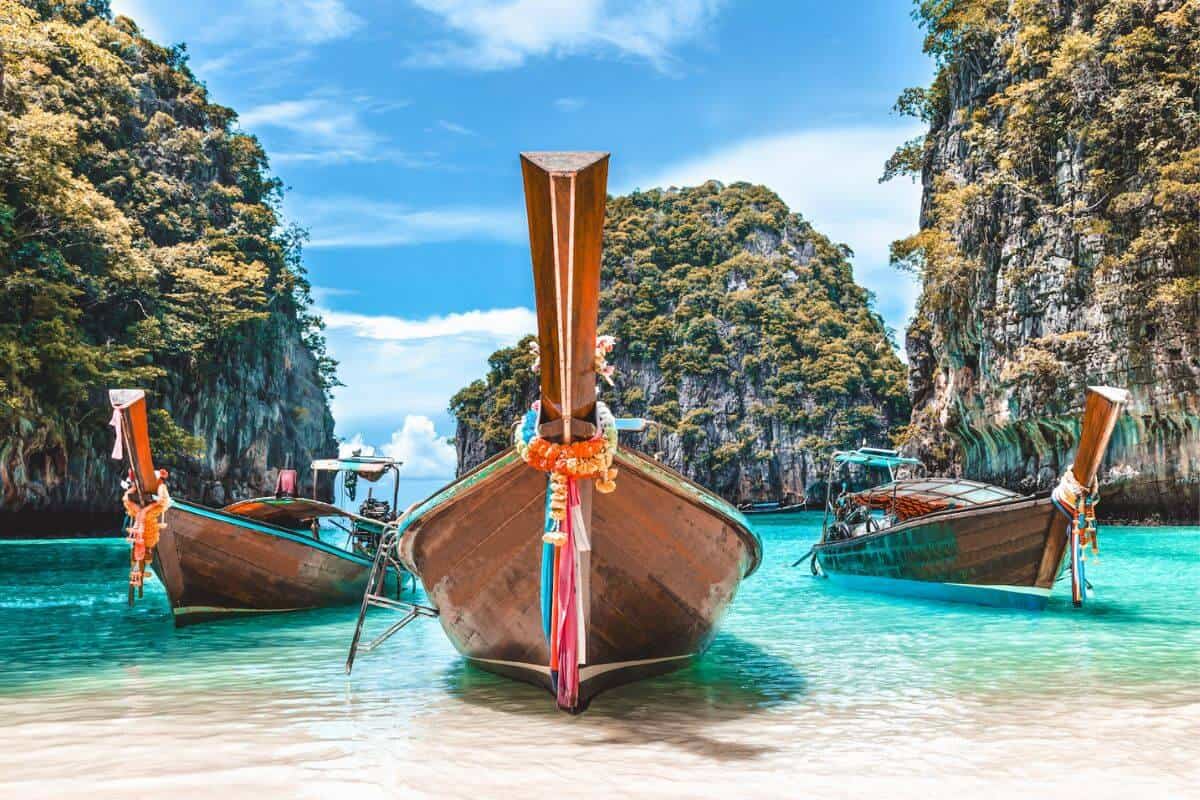 Three wooden longtail boats in shallow sea surrounded by limestone cliffs in Thailand