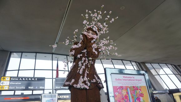 Person in a floral costume at an airport terminal with a sign for Dulles International Airport.