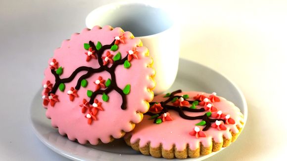 Pink cookies with cherry blossom design and a white cup in the background.
