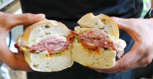 Person holding a ham and cheese sandwich with lettuce and tomato.