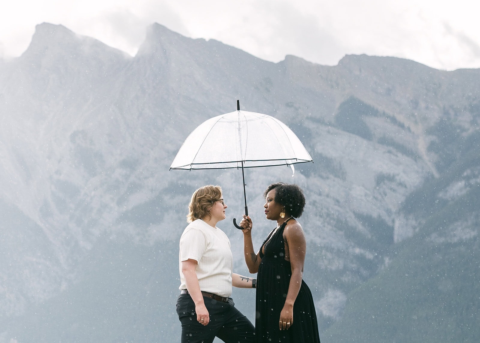 Couple taking Kananaskis engagement photos at a mountain lake with dramatic peaks in the background