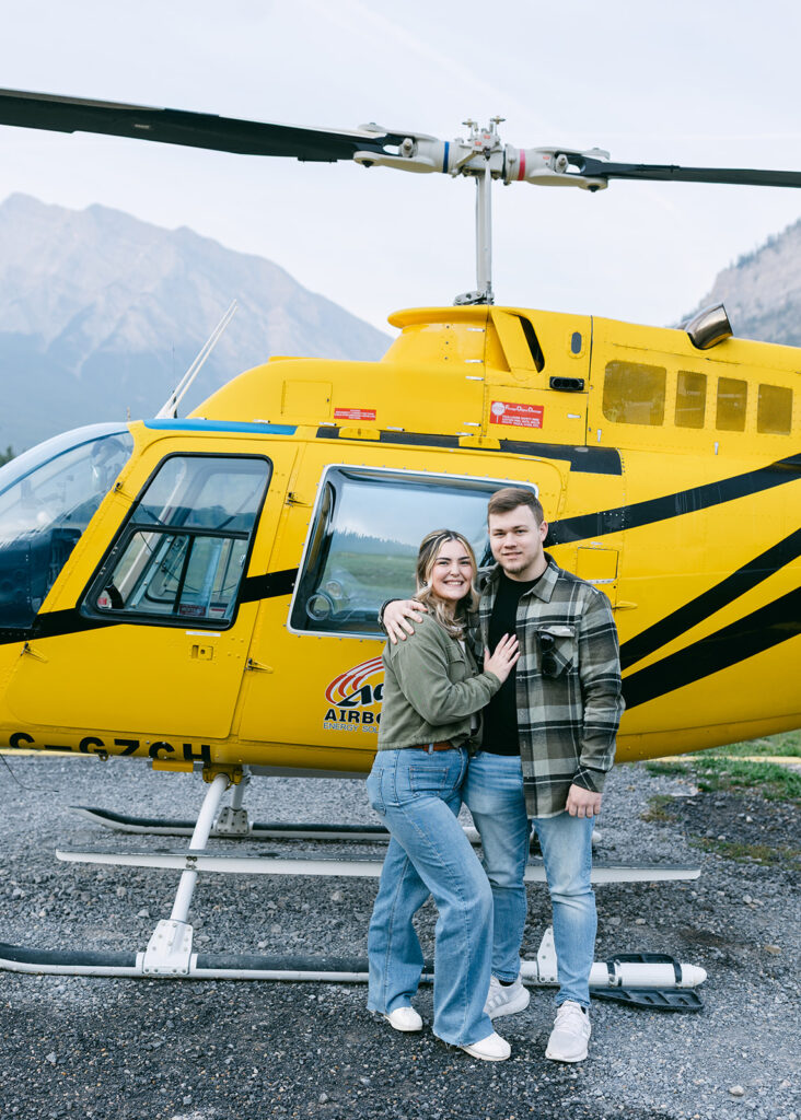 Adventurous heli proposal with a couple standing beside a helicopter on a rugged alpine peak