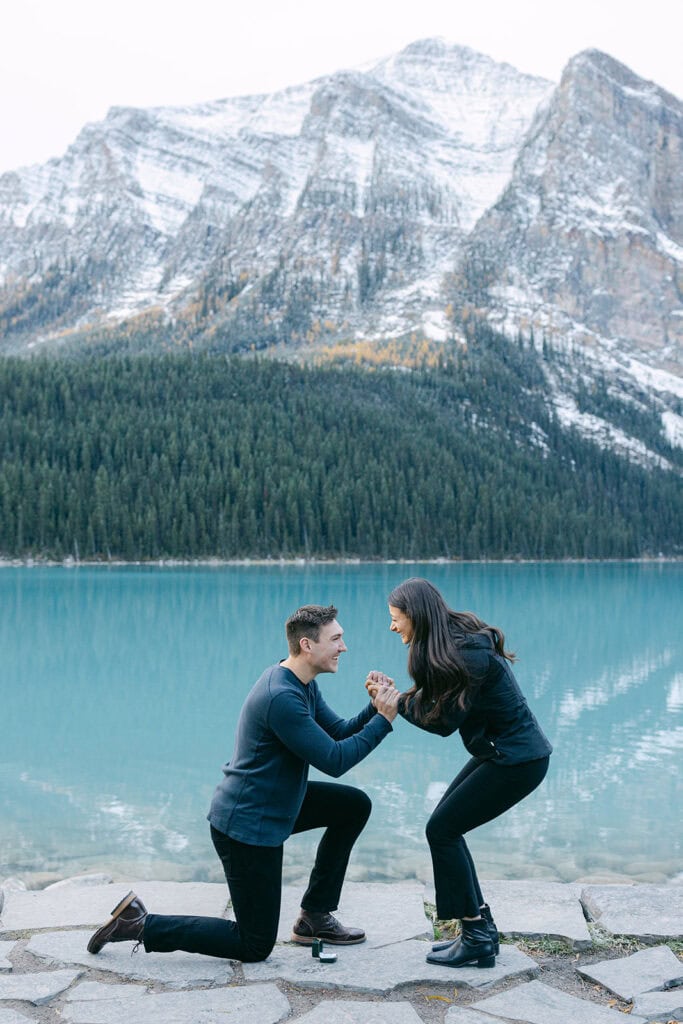 Couple during a Lake Louise engagement with blue glacier lake, golden autumn trees, and snowy mountain tops