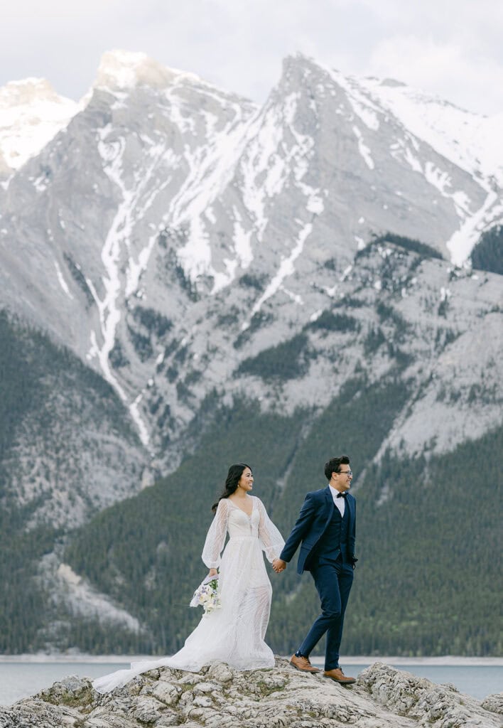 Lake Minnewanka elopement couple walking along rocky lakeshore in Banff