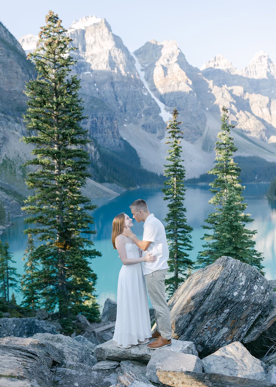 Scenic engagement photos at Moraine Lake with dramatic mountain backdrop, reflective water, and natural candid couple portraits