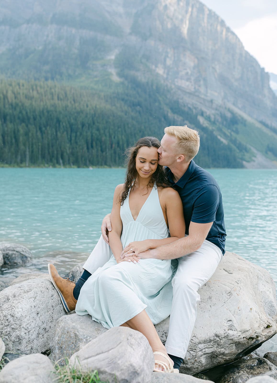 Couple embracing by turquoise water during Lake Louise engagement photos in Banff National Park