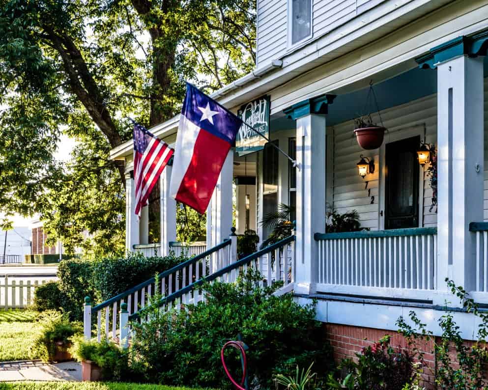 A white house with an American flag and a Texas state flag that benefits from the Texas FAIR plan.