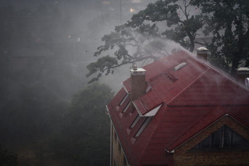 An image of heavy rain beating down on the roof of a large home with a red roof