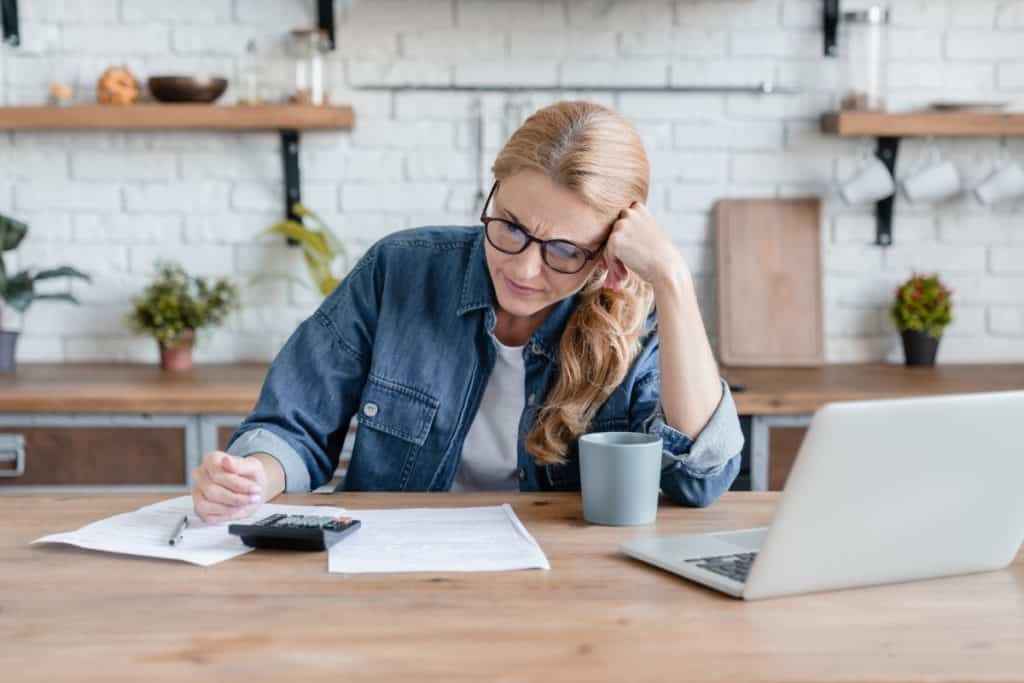 Frustrated woman reviewing documents at kitchen table, concerned about insurance coverage disputes after a denied claim.