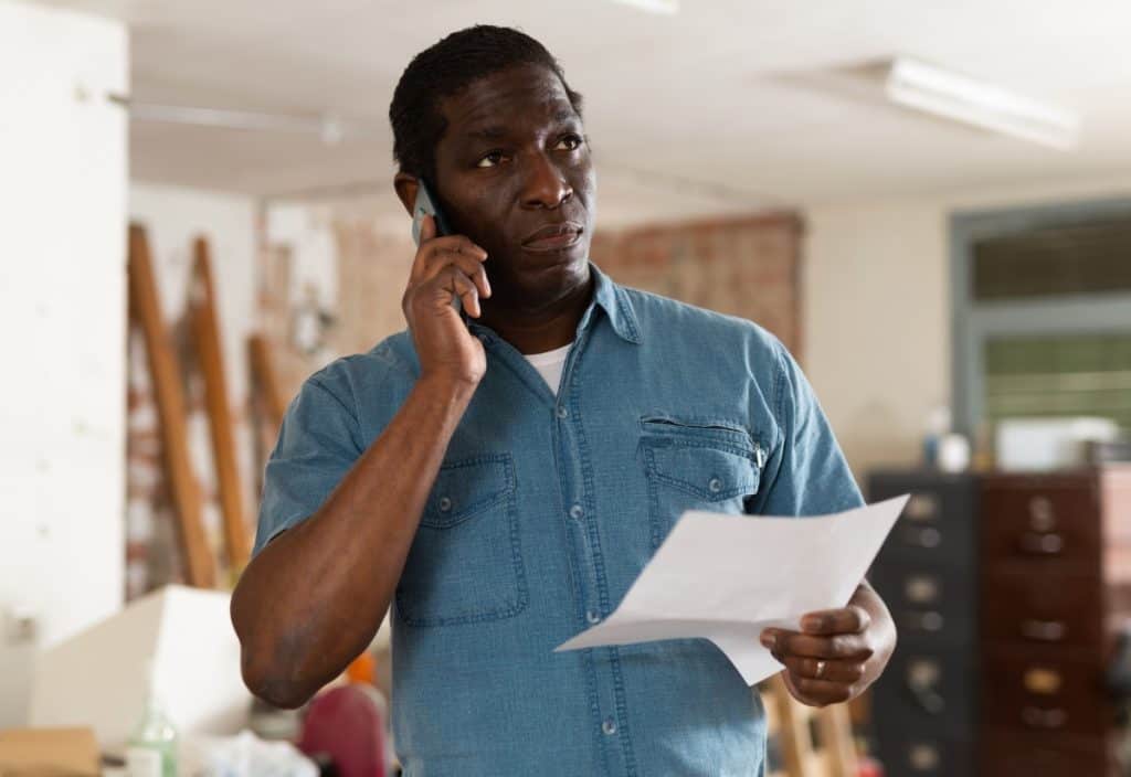 Concerned man on phone holding paperwork and discussing a denied hurricane insurance claim.