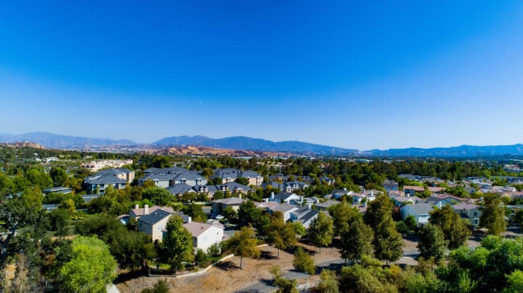 Aerial view of a suburban neighborhood in California surrounded by dry hills and vegetation, highlighting areas at risk for wildfires and relevant to wildfire insurance claims in California.