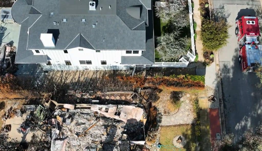 Aerial view showing a home spared next to a neighboring property destroyed by wildfire, illustrating the importance of filing a wildfire insurance claim for property damage and loss even when your home doesn't burn down.