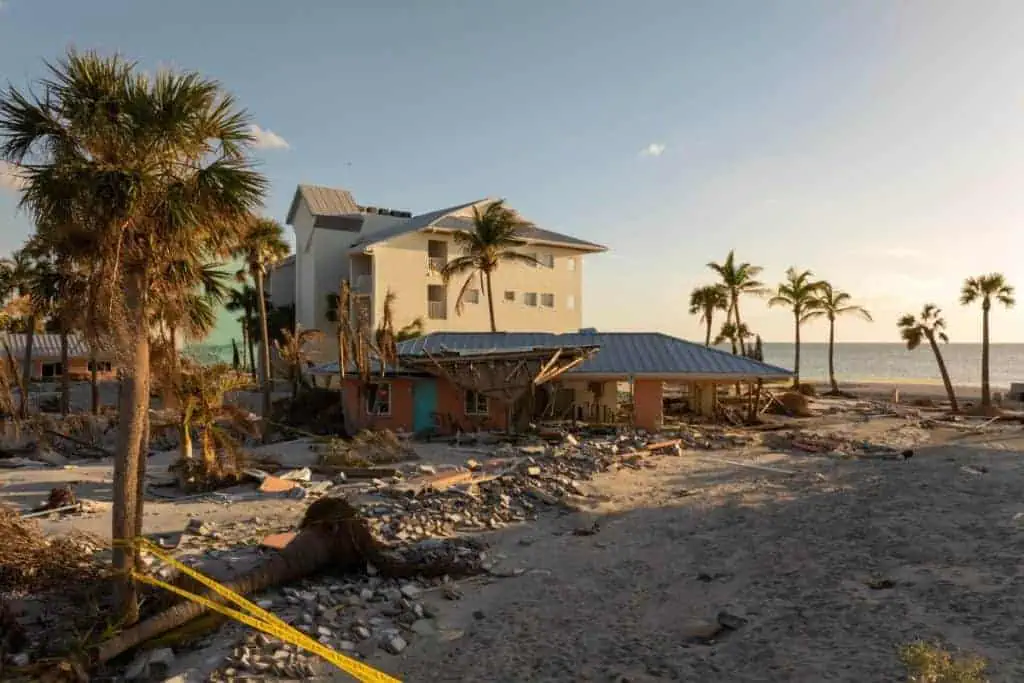 A beachfront property in Florida shows severe storm surge damage with fallen palm trees, debris, and destroyed buildings, illustrating the importance of having Florida flood insurance after hurricanes.