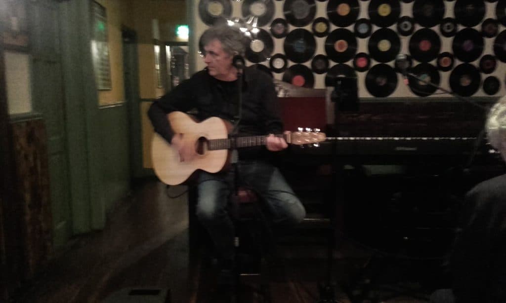 Musician playing acoustic guitar during a live music session at a cosy venue.