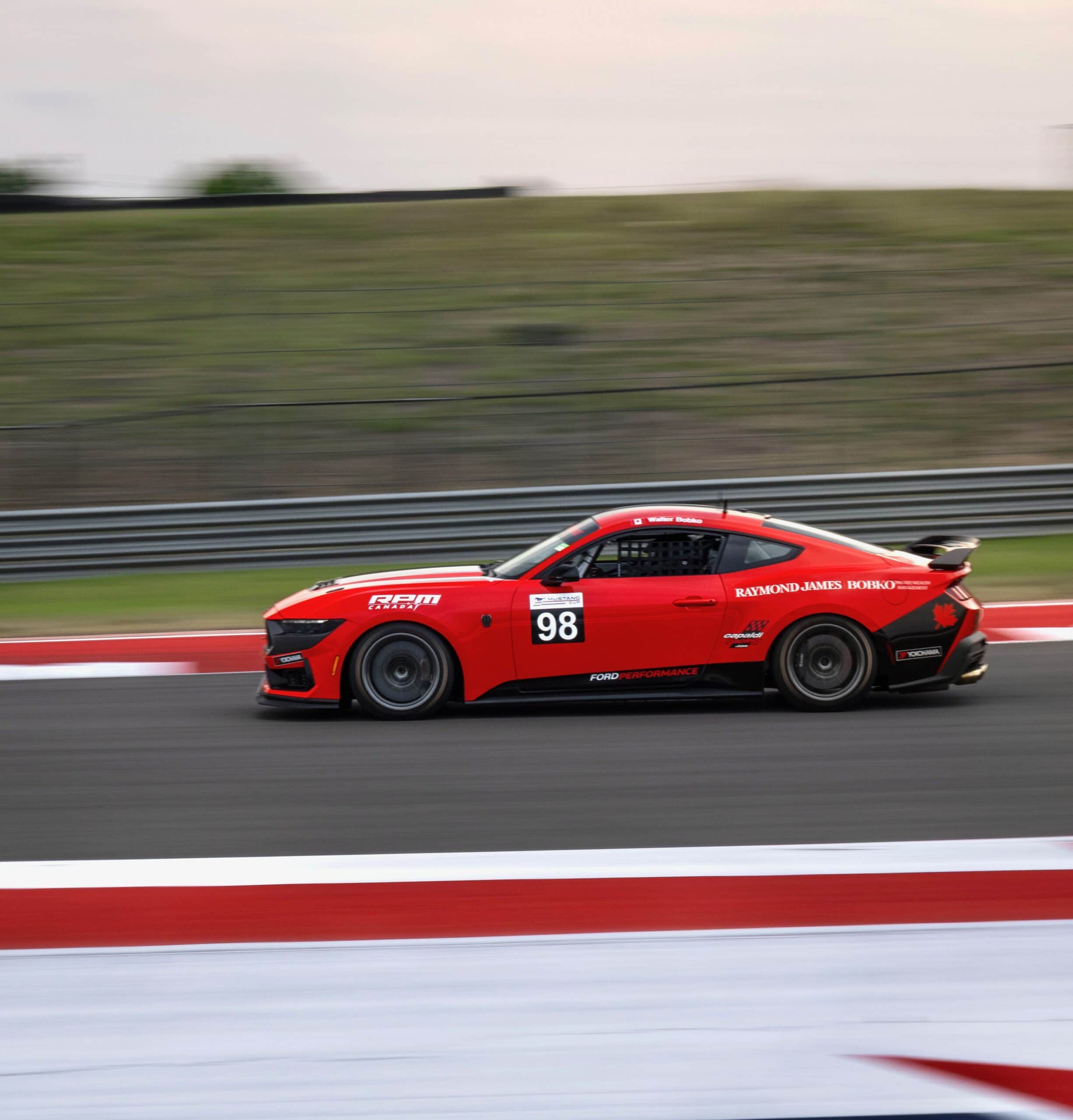 Red Mustang race car on track during Mustang Week event.