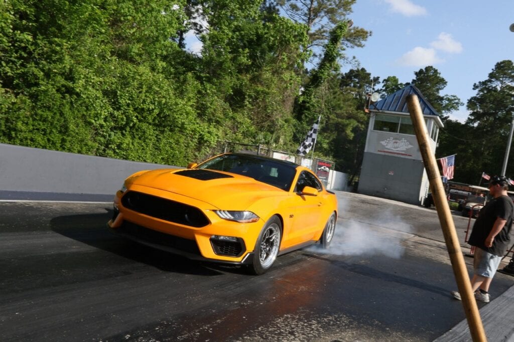 Yellow Ford Mustang performing a burnout at zMAX Dragway during Mustang Week.