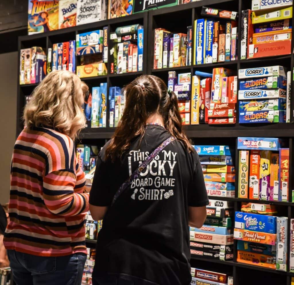 Two women browsing board games on a store shelf at Mustang Week.