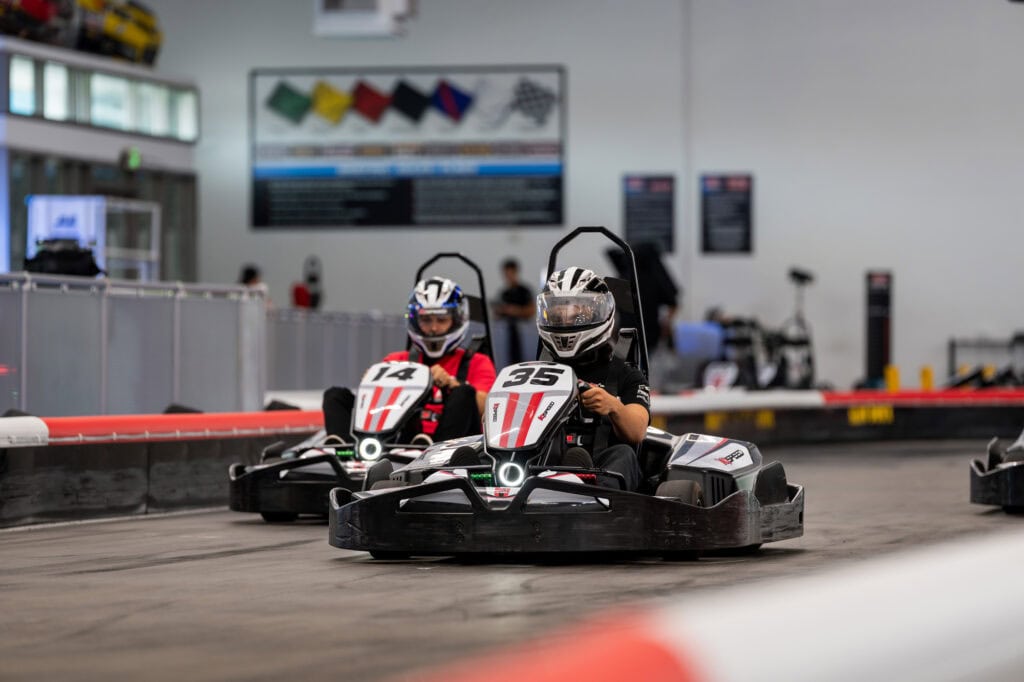 Two kids racing go-karts indoors at Mustang Week event.